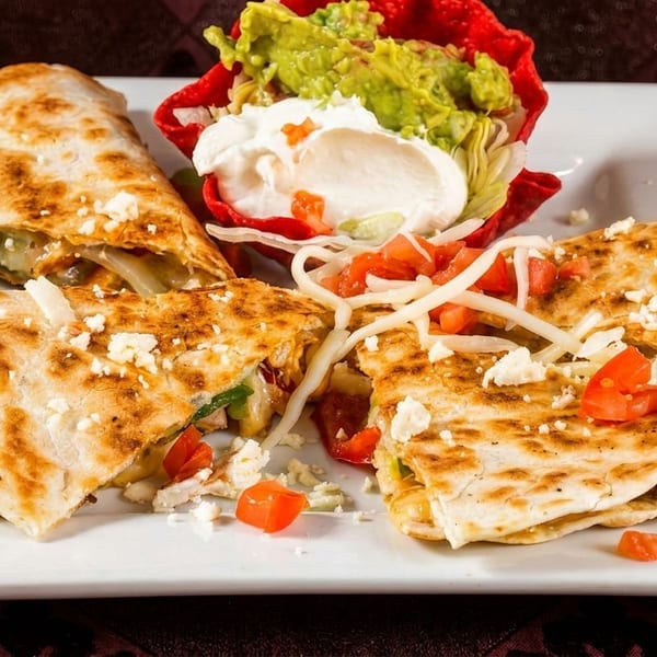 Chicken quesadillas with guacamole, sour cream, and pico de gallo on a white plate.