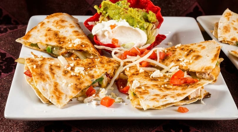 Chicken quesadillas with guacamole, sour cream, and pico de gallo on a white plate.