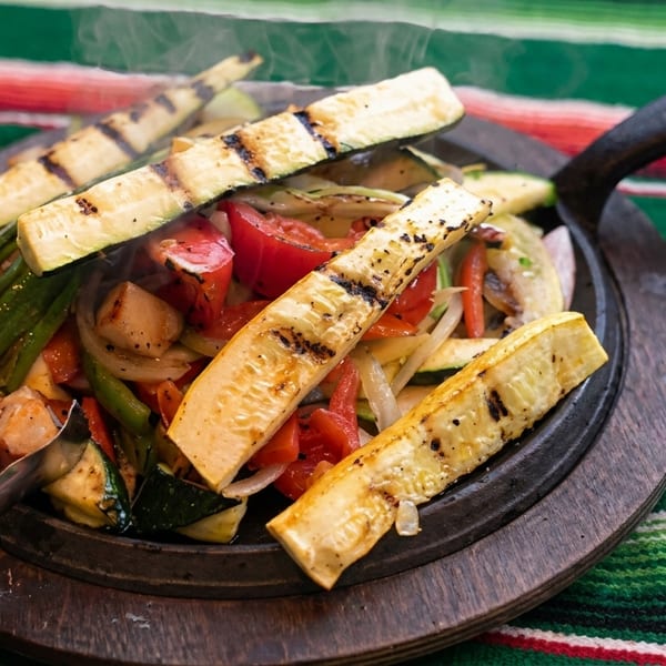 Sizzling fajitas with grilled zucchini, bell peppers, onions, and chicken on a wooden platter.