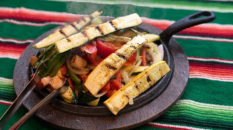 Sizzling fajitas with grilled zucchini, bell peppers, onions, and chicken on a wooden platter.