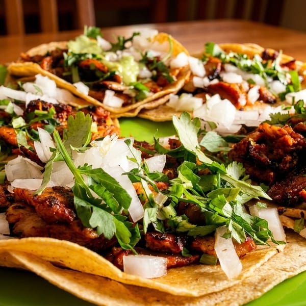 A vibrant green plate holds several street tacos topped with meat, onions, cilantro, and a lime wedge.